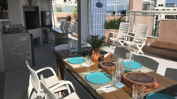 An outdoor dining area with a wooden table set for four, surrounded by white chairs.