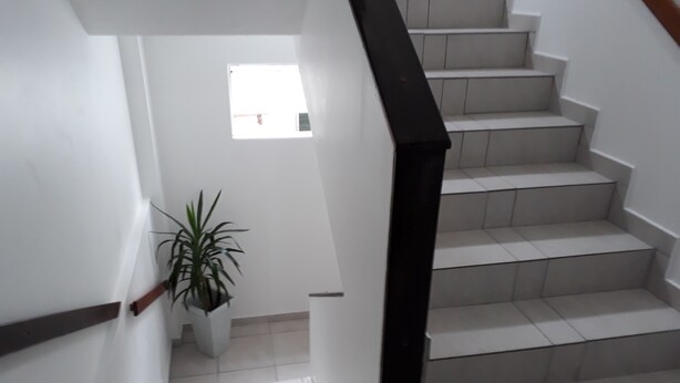 Eine Treppe mit weißen Fliesen und einem schwarzen Geländer führt zu einer Zwischenebene. Dort steht ein Blumentopf.