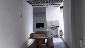 Ein schmaler Korridor mit gefliestem Boden, ein kleiner Tisch mit einer Kiste darauf, ein Fernseher an der Wand und eine Küchenzeile im Hintergrund.