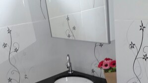 Ein Badezimmer mit einem weißen Waschbecken, einer schwarzen Arbeitsplatte und einem Spiegel darüber. Auf der Arbeitsplatte befinden sich dekorative Wandsticker und eine kleine Vase mit Blumen.