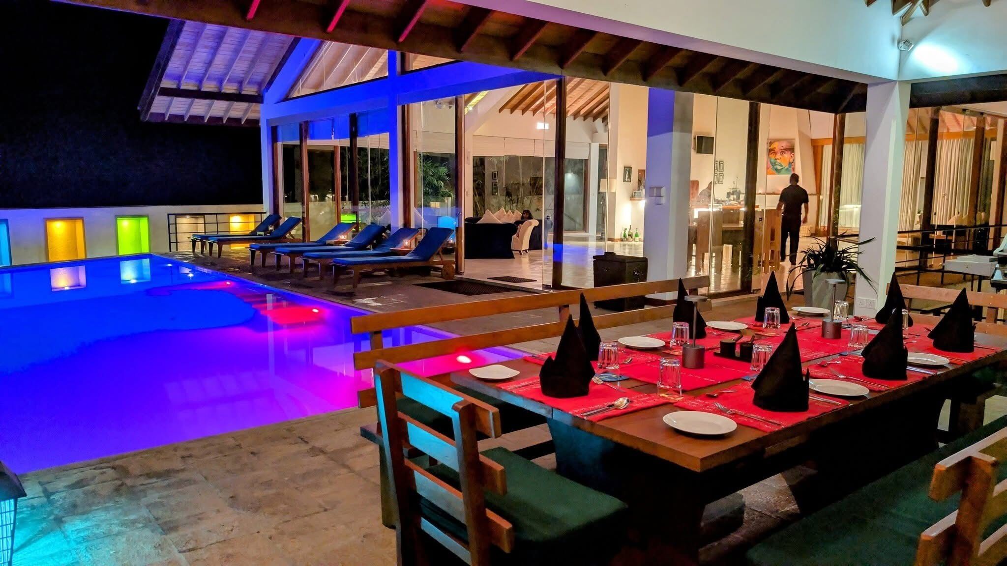 A poolside dining area with tables set for two, lounge chairs, and a view of the pool.