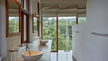 Un baño con un lavamanos grande, un espejo y vistas a un paisaje verde y exuberante a través de una puerta de cristal.