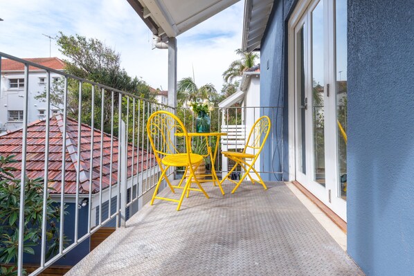 A balcony with yellow chairs and a table, overlooking a residential area with red-roofed houses. - Charming, spacious boutique apartment 200 metres from Bondi Beach (Bondi Beach)