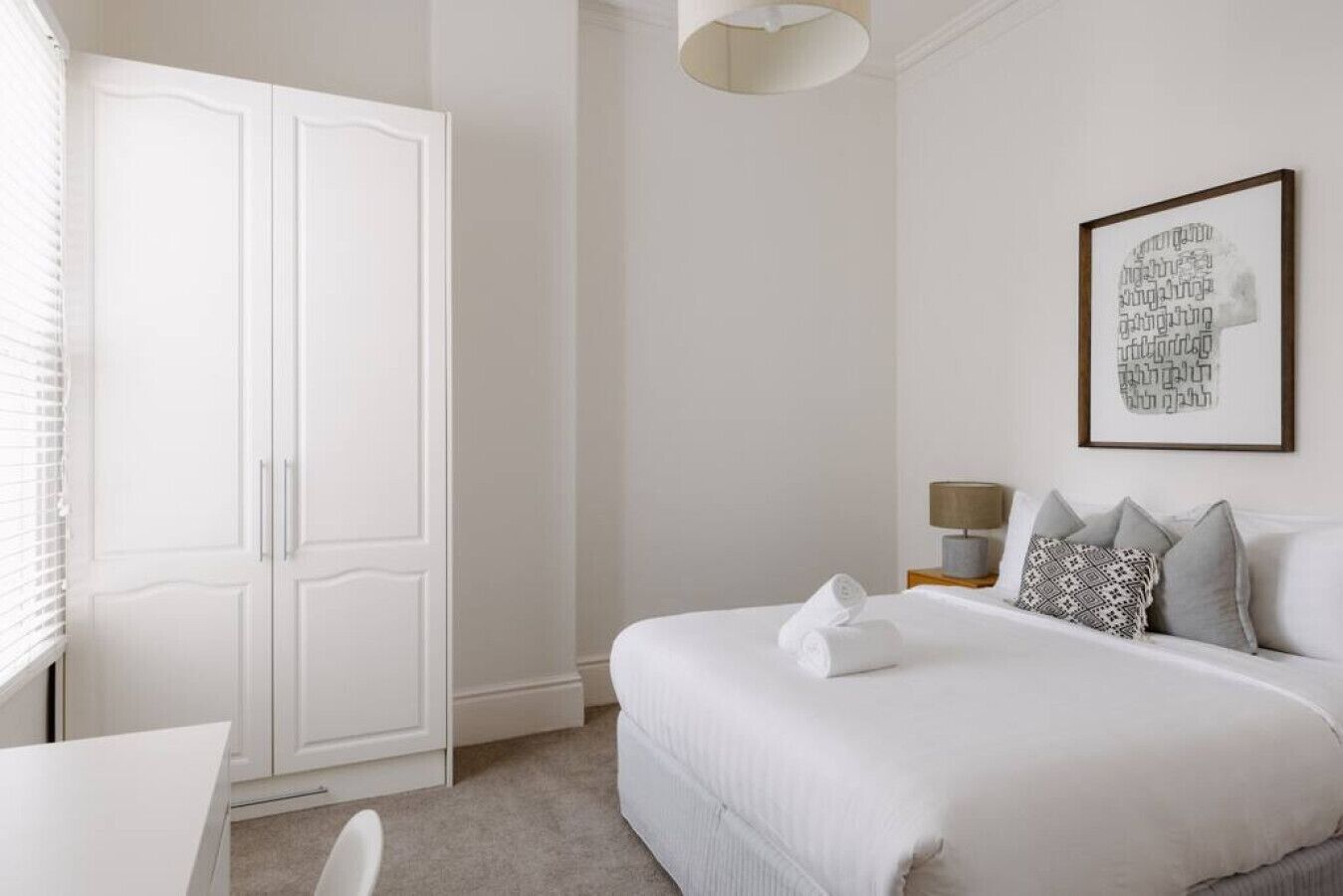 Camera d'albergo con un letto grande, un comodino con una lampada, un armadio e un'opera d'arte appesa al muro.