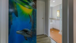 Un pasillo con un mural llamativo de delfines y olas, que conduce a un baño con elementos blancos y piso de baldosas.