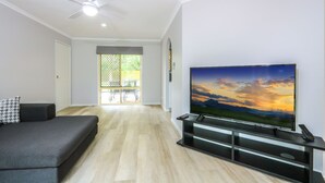 Una sala de estar moderna con televisor de pantalla plana, ventilador de techo y puerta corrediza de vidrio que da a un patio.