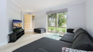 Una sala de estar moderna con un sofá grande, una mesa de centro de vidrio y un televisor de pantalla plana sobre un mueble.