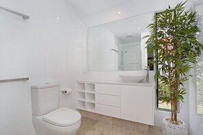 A modern bathroom with a toilet, a large mirror, a sink, and a potted plant. - Seaclusion Broadbeach – Effortless Luxury, Coastal Calm (Gold Coast)