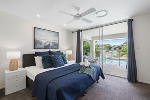A bedroom with a bed, a ceiling fan, a nightstand with a lamp, a large window, and a view of a swimming pool. - Seaclusion Broadbeach – Effortless Luxury, Coastal Calm (Gold Coast)