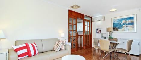 A modern living room with a sofa, a small round table, and a dining area with chairs.