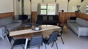 A cozy living room with a wooden table, two grey sofas, and a black armchair. - Rustic cabin & large kitchen block nestled in a native garden. (Western Lake, Featherson)