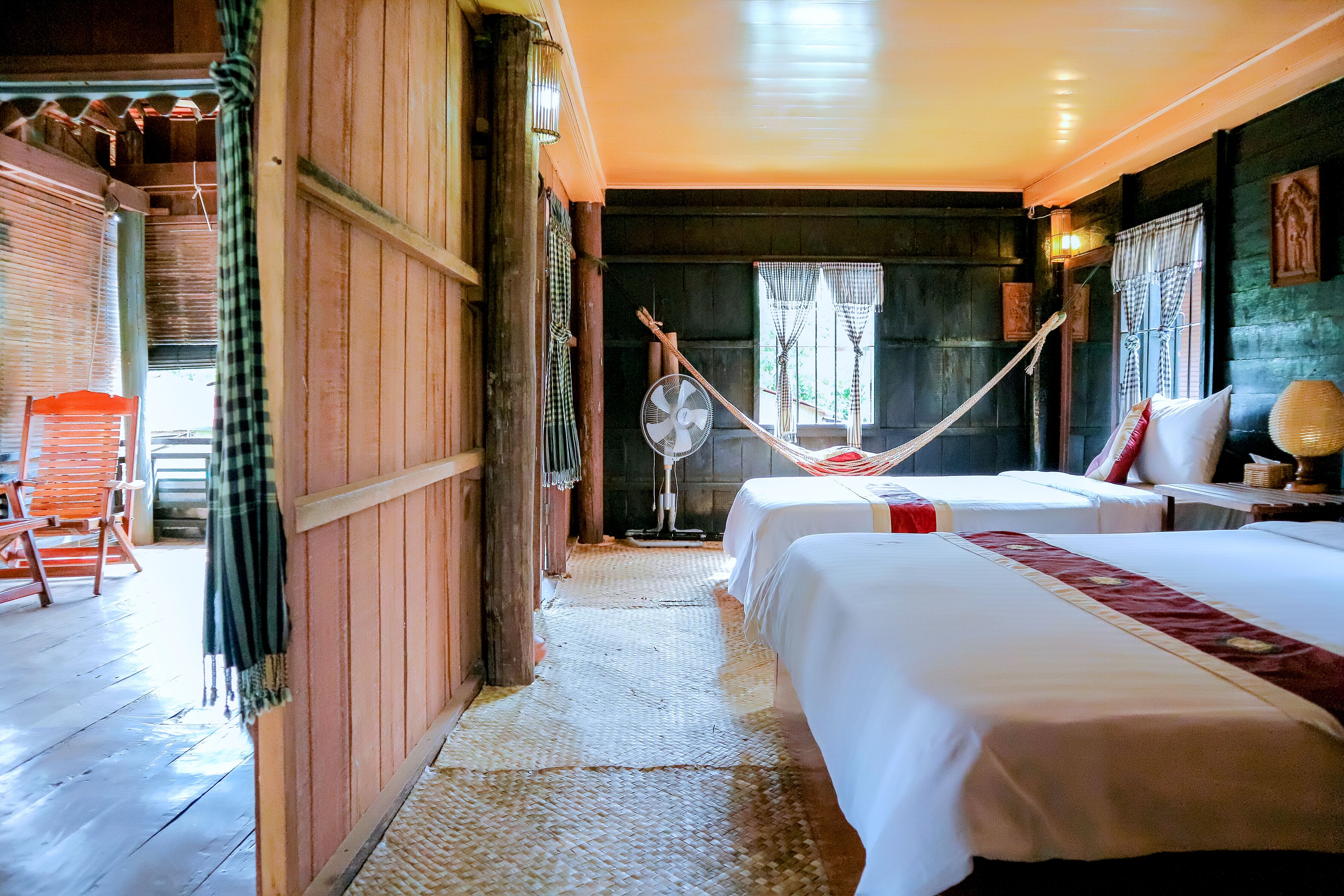 A room with two beds, a fan, and a hammock.