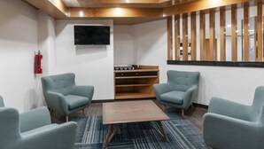 A modern waiting area with four grey armchairs, a wooden coffee table, and a flat-screen TV mounted on the wall. - Hotel San Lucas (Mexico City)