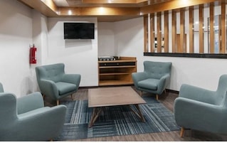 A modern waiting area with four grey armchairs, a wooden coffee table, and a flat-screen TV mounted on the wall.