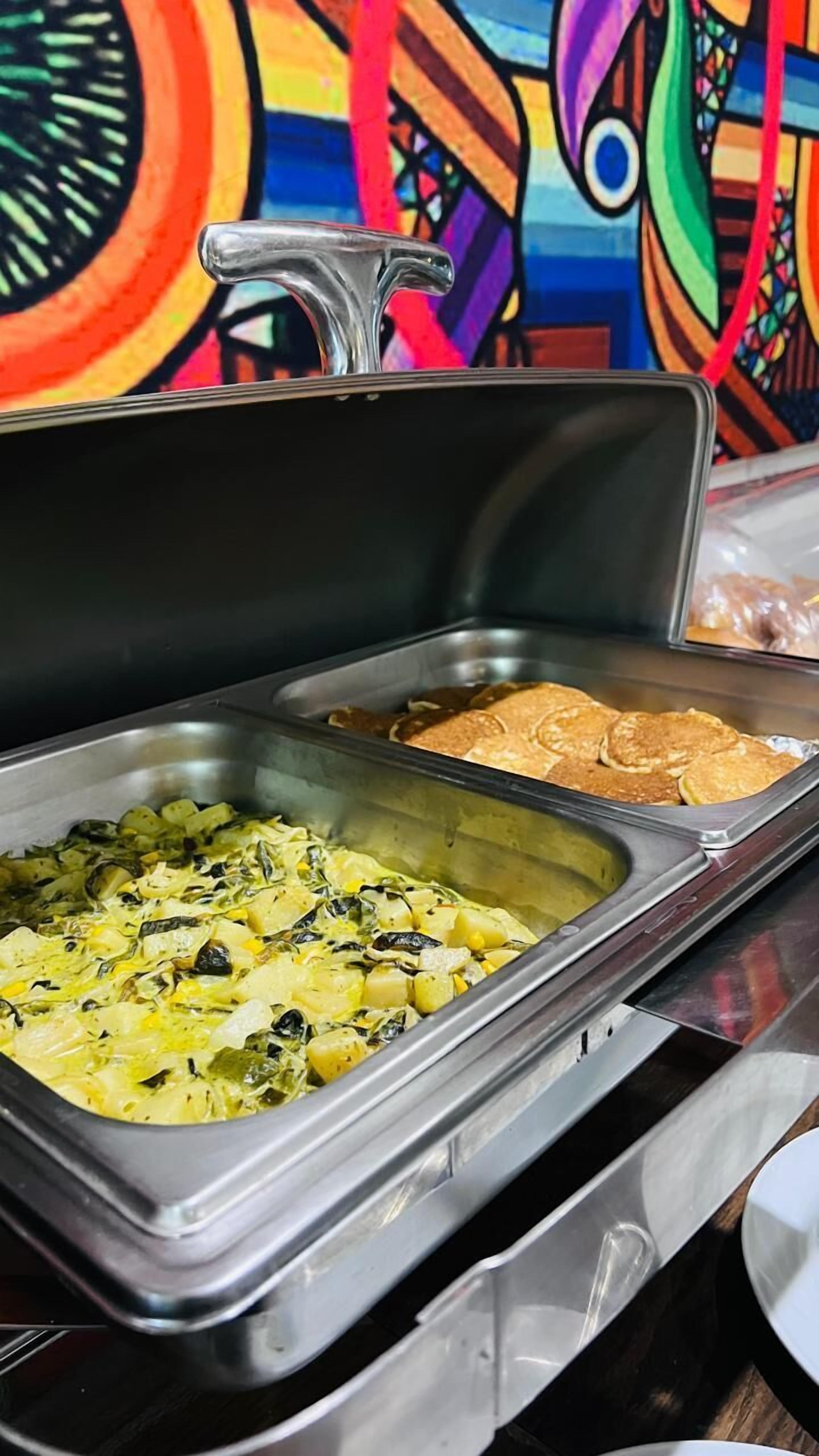 Ein reichhaltiges Buffet mit verschiedenen Speisen, darunter Salat und Pfannkuchen, in einem Raum mit einer farbenfrohen Wandmalerei.