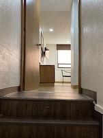 A wooden staircase leading to a room with a desk and chair, a framed picture on the wall, and a window with blinds.