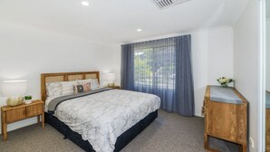 A bedroom with a bed, nightstands, a wooden bench, and a window with curtains.