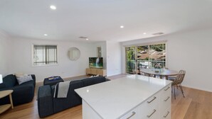 A modern living room with a sofa, a coffee table, and a TV. There is a balcony with a table and chairs.