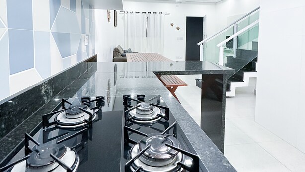 A modern kitchen with a central island, black countertops, and a gas stove. - House for vacation in Maranduba/Ubatuba (Maranduba)