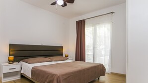Quarto com cama, mesas de cabeceira, ventilador de teto e janela com cortinas.