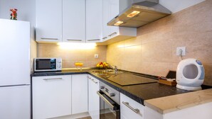 Uma cozinha moderna com armários brancos, micro-ondas, chaleira e uma fruteira com laranjas.