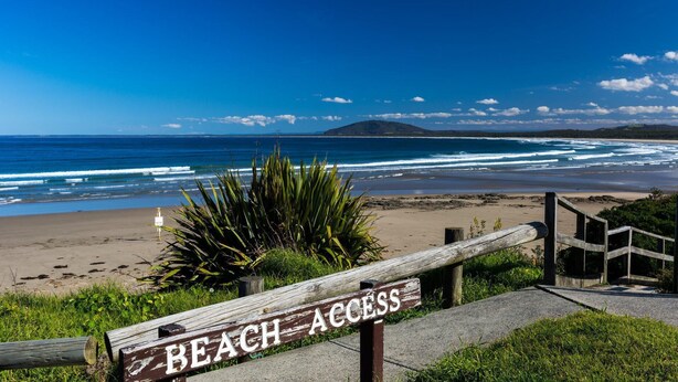 Een houten bord met de tekst 'BEACH ACCESS', met uitzicht op de oceaan en een berg op de achtergrond.