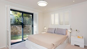 Een slaapkamer met een groot bed, een schuifdeur naar een tuin, witte muren en een plafondlamp.