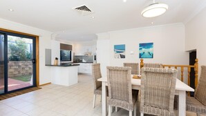 Een moderne keuken met witte kasten, een centraal eiland en een eethoek met rieten stoelen en een witte tafel.