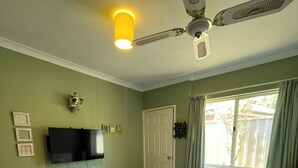 A bedroom with a large bed, a ceiling fan, a flat-screen TV mounted on the wall, and a window with curtains.