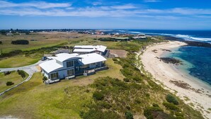 Une propriété située sur la côte, avec une grande maison comprenant de nombreuses pièces et un balcon, le tout entouré d’un paysage luxuriant et donnant sur une plage.