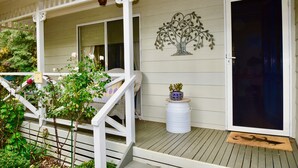 Ein Holzdeck mit weißer Brüstung, einem Blumentopf und einem dekorativen Metallbaum.