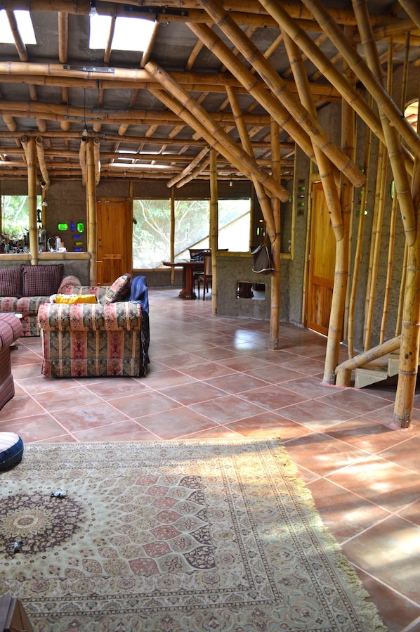 Una habitación amplia con un techo alto de bambú, una alfombra estampada y un sofá con una manta.