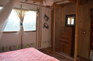 A bedroom with a bed, a window with curtains, a wooden wardrobe, and wall decorations. - Casa Bambú - Amplia y acogedora, ubicada dentro de una granja ecológica (Lechuguillas)