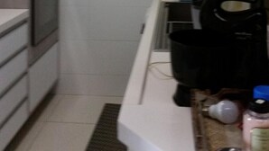 Une cuisine étroite avec des meubles blancs, un four à micro-ondes et une machine à café posés sur le plan de travail.