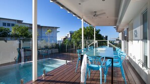 A covered outdoor area with a pool, blue chairs, and a table.