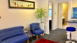 A modern living room with a blue sofa, a small round table, a red rug, and a framed picture of deer on the wall. - Amber Homes B Half Moon Bay (Bucklands Beach)
