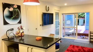 A modern kitchen with a black countertop, white cabinets, a red pendant light, a clock, and a sliding glass door leading to a patio. - Amber Homes B Half Moon Bay (Bucklands Beach)