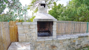 Un forno esterno in pietra con canna fumaria, circondato da una recinzione in bambù e un muro in pietra.