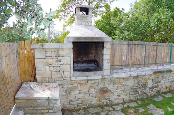 Un horno de piedra al aire libre con chimenea, rodeado por una cerca de bambú y un muro de piedra.