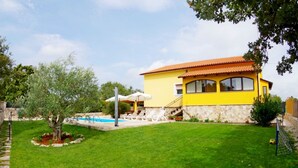 Una casa gialla con piscina, un albero e un muro in pietra.