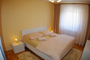 Un dormitorio con cama, lámparas de noche, mesita de noche y ventana con cortinas.