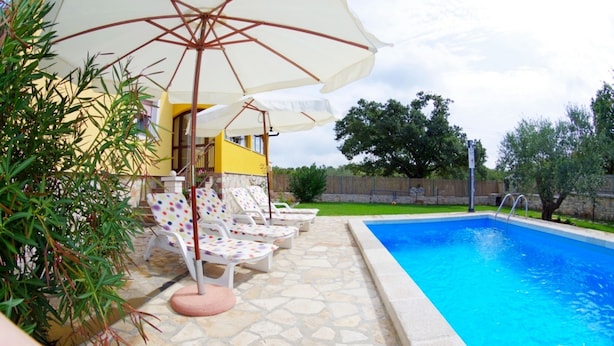 Una piscina con lettini e ombrelloni, circondata da un patio in pietra e vegetazione.