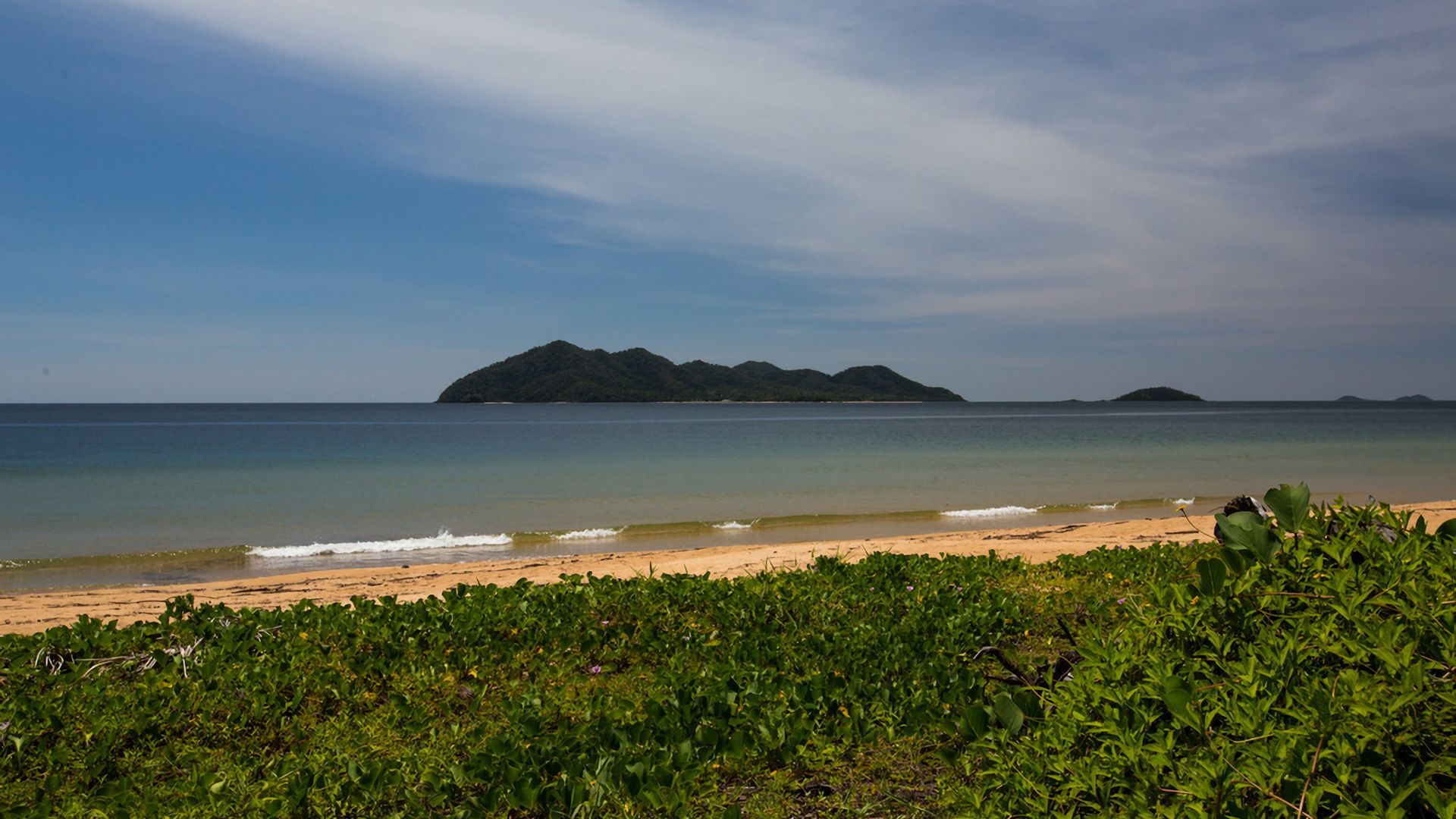 Una playa con agua cristalina, una orilla arenosa e islas verdes a lo lejos.