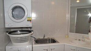 A compact laundry area with a front-loading washing machine, a stainless steel sink, and a white basin.