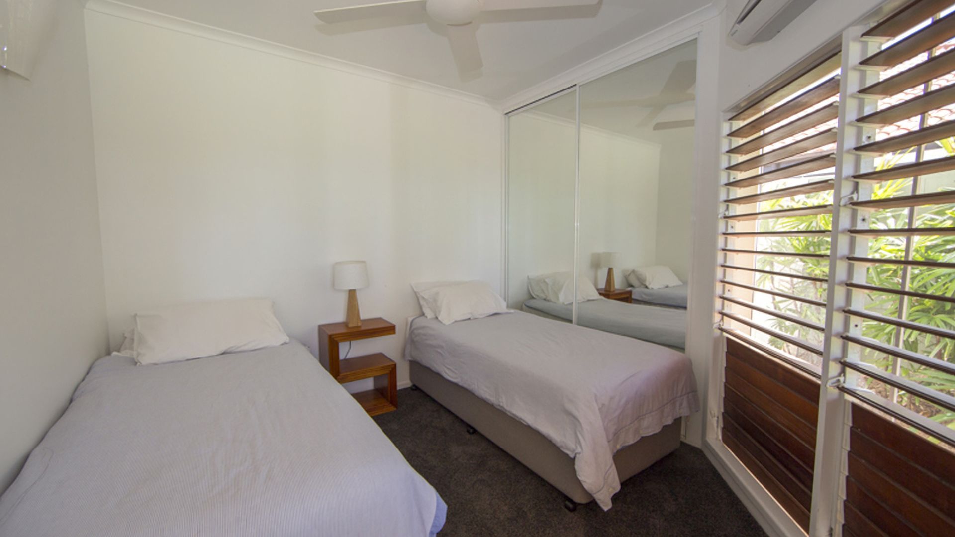 A bedroom with two single beds, a ceiling fan, and a large window with blinds.