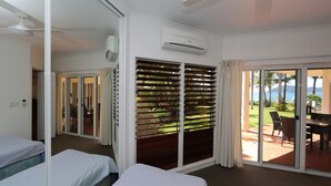 A hotel room with two beds, a sliding glass door to a balcony, an air conditioning unit, and a ceiling fan.