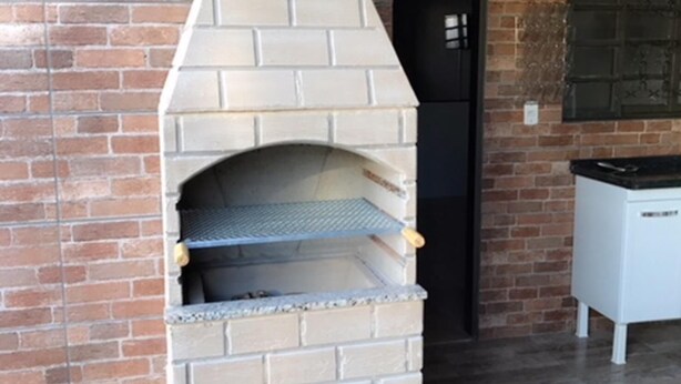 Ein Backofen aus Ziegelsteinen mit Schornstein, ein Fliesenboden und ein Küchenbereich mit Kühlschrank und Schränken.