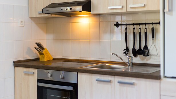 Een keuken met lichte houten kastjes, een roestvrijstalen spoelbak en een messenblok.