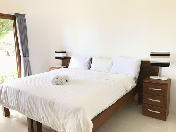 Un lit bien fait, avec du linge de lit blanc, deux tables de chevet avec des lampes et une fenêtre avec des rideaux.