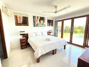 A bedroom with a bed, bedside tables, a ceiling fan, and a view of a swimming pool.